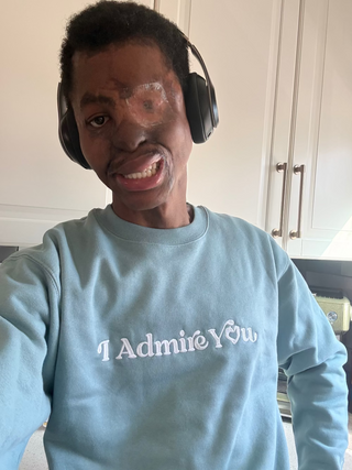 Joshua Dixon wearing a light blue sweatshirt with 'I Admire You' text, indoors.